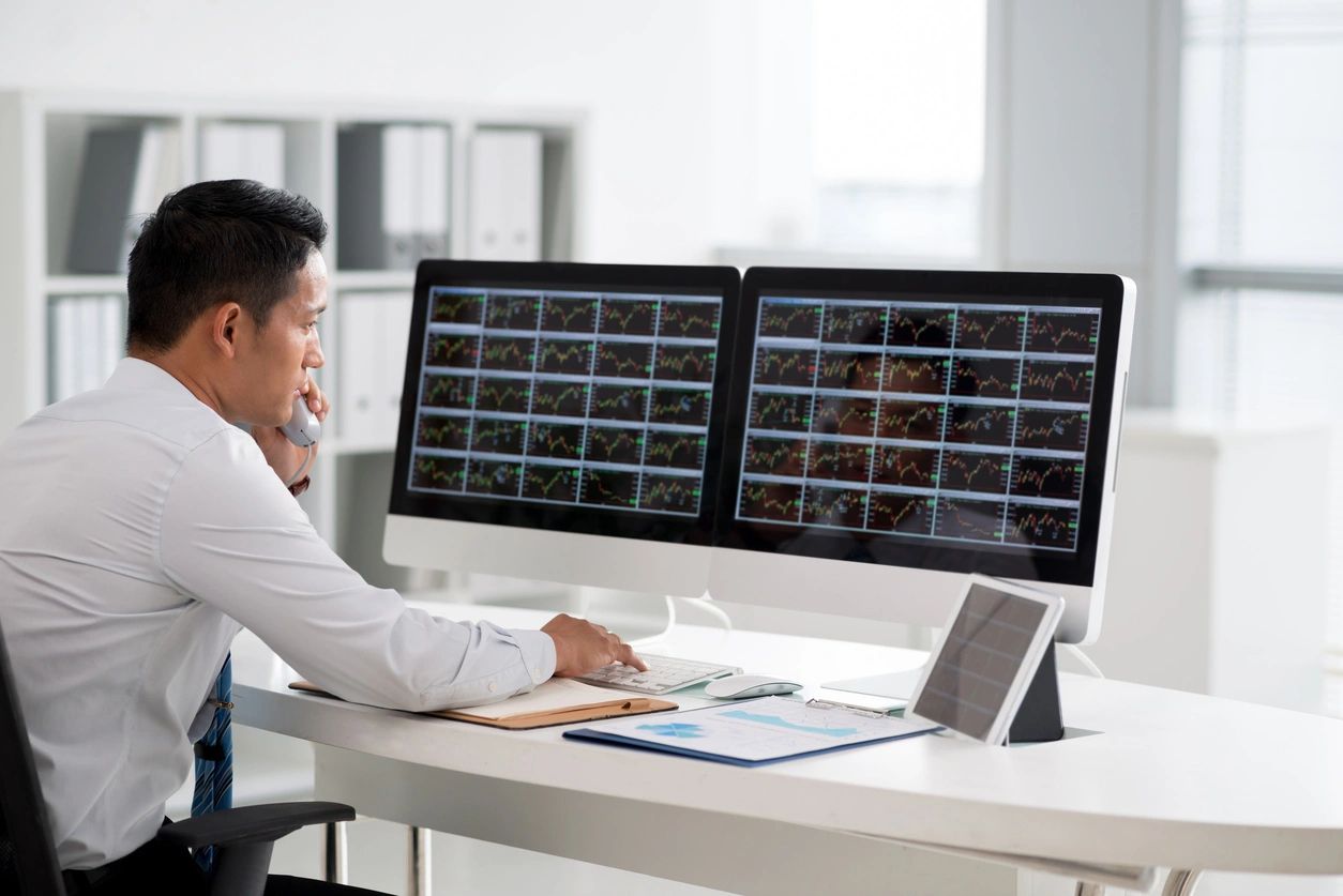 A man sitting at his desk looking at two monitors.